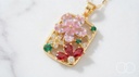 Close up of the Garden Panel pendant: pink crystal flower, red marquise petals and green rounds in a gold openwork panel