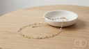 The Rainbow Bead necklace on a pale wood table beside a ceramic dish